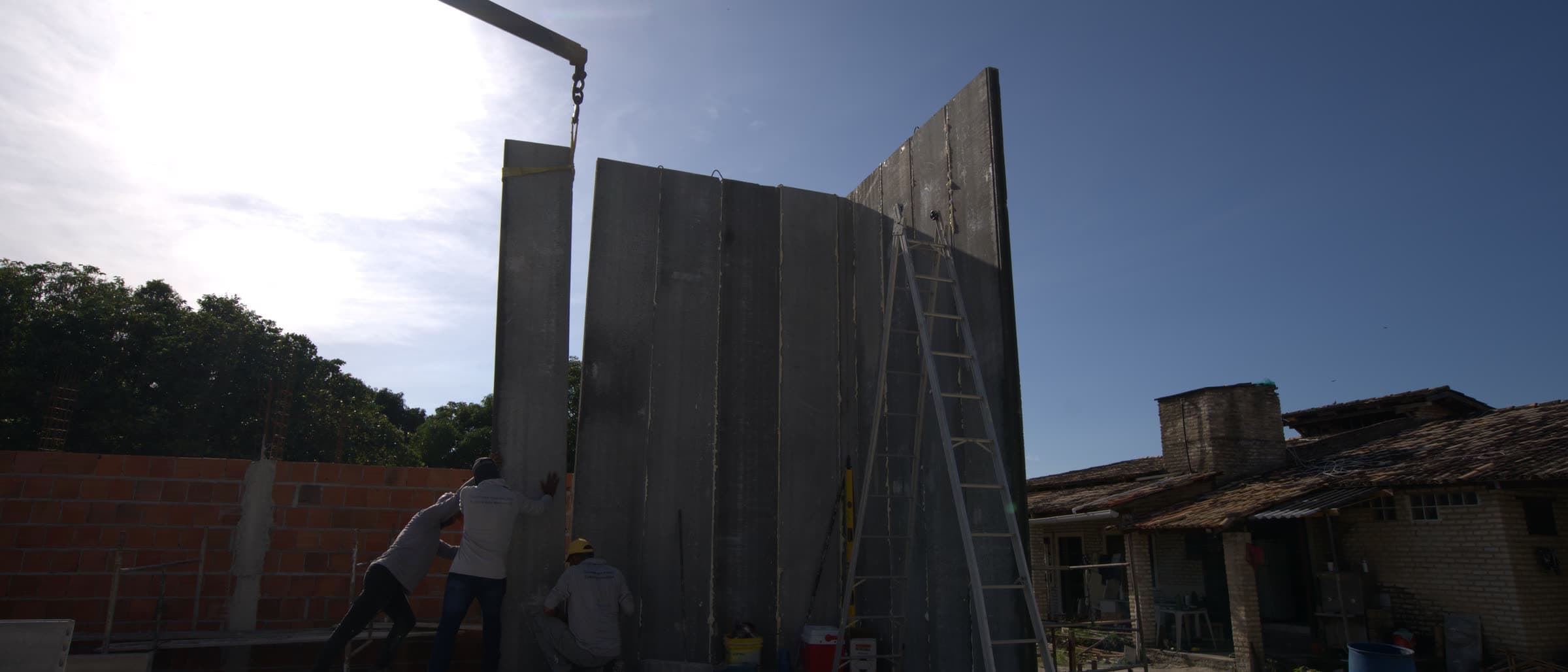 Guindaste posicionando um painel de parede de concreto pré-moldado ao pôr do sol em uma obra da A Fábrica das Casas